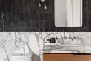 Floating wood vanity with marble backsplash and black handmade Zellige wall tile in modern guest bath.