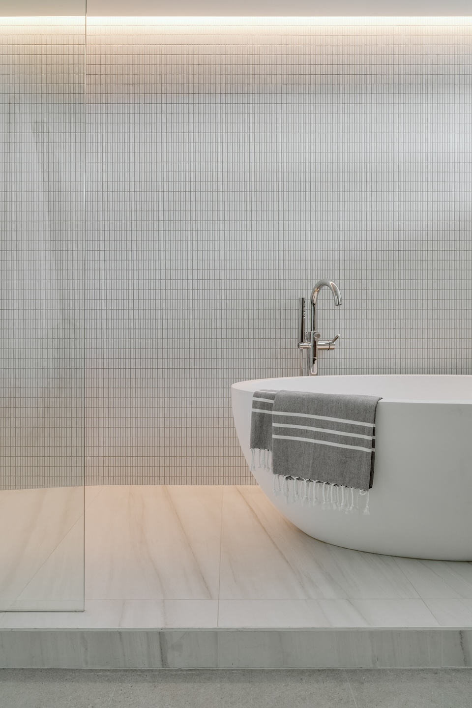 Refined minimalist bathroom design in Fort Lauderdale featuring a sculptural soaking tub, grid tile wall, and integrated LED lighting by STUDIO 818.